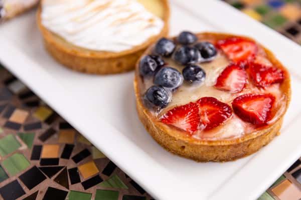 Fruit tart topped with fresh strawberries and blueberries glazed over cream filling, served on a white rectangular plate