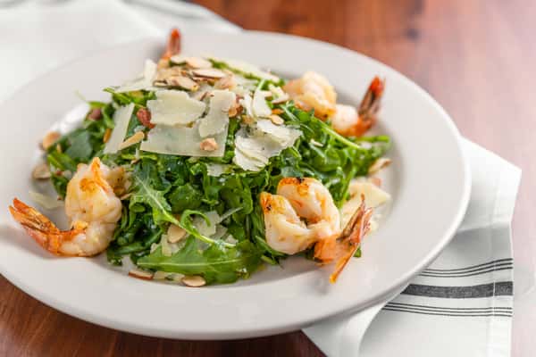 Grilled shrimp and arugula salad topped with shaved Parmesan and sliced almonds on white plate