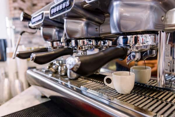 Close-up of a commercial espresso machine dispensing fresh espresso into two small white cups on a metal drip tray.