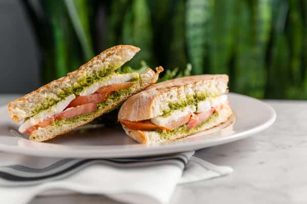 Caprese sandwich with pesto, fresh mozzarella, and tomato on toasted ciabatta, served on white plate
