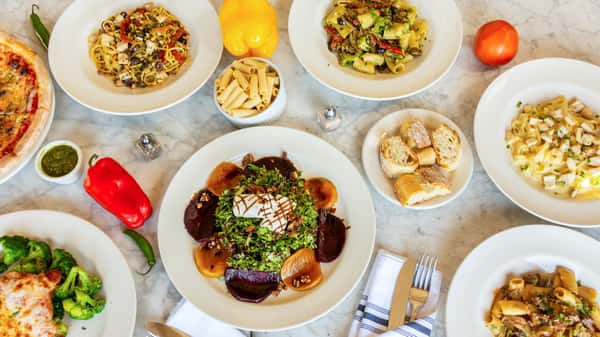 Overhead view of assorted Italian dishes, pasta, pizza, salad, and bread on a marble table with fresh vegetables.