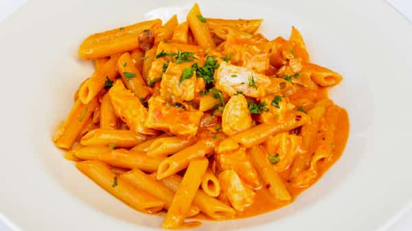 Penne pasta in creamy tomato sauce with grilled chicken, mushrooms, and parsley garnish in white bowl