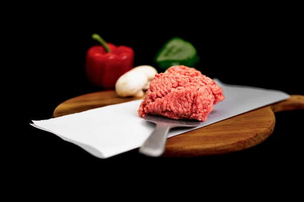 fresh ground beef on butcher paper with vegetables on wooden cutting board