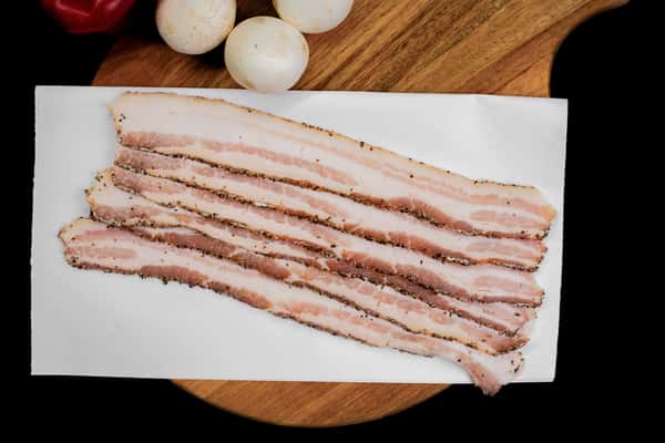 sliced peppered bacon strips laid out on butcher paper with seasoning visible
