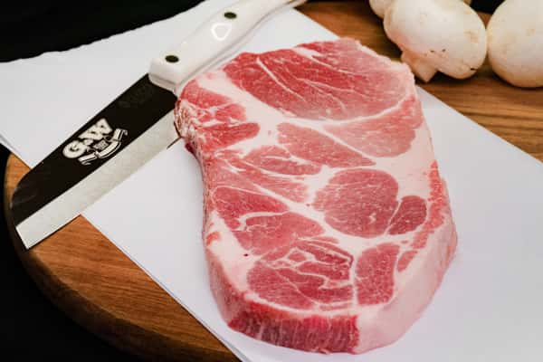 raw pork steak with marbling on cutting board next to knife in butcher prep setting
