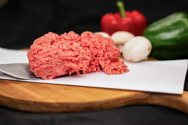 fresh ground beef on butcher paper with peppers and onions on wooden board