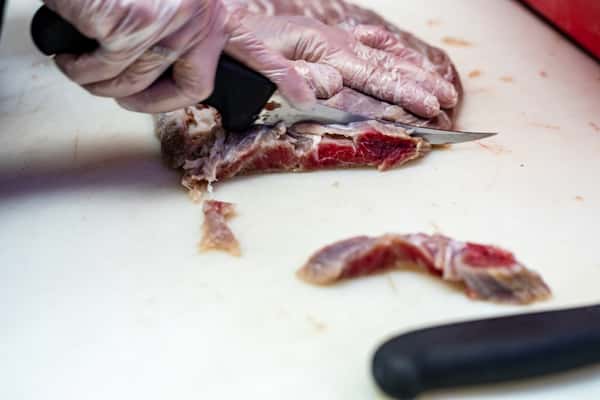 butcher slicing fresh meat on cutting board inside G&W Sandwiches prep area