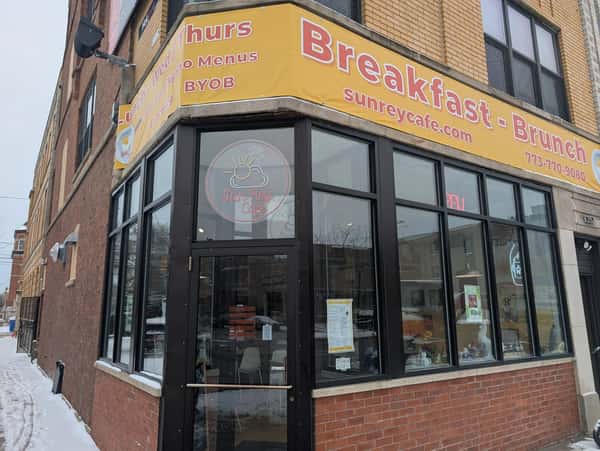 Street view of Sun Rey Cafe with large yellow banner advertising breakfast and brunch, and glass door entrance with logo.