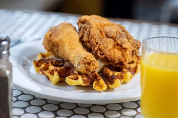 Plate of chicken and waffles served with a glass of orange juice on the side.
