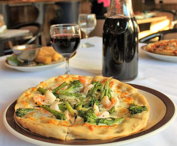 Gamberetti Pizza: topped with broccoli and shrimp on the table with a glass and carafe of wine