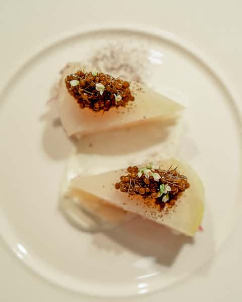 Gourmet dish featuring two delicately plated pieces of fish topped with caviar, herbs, and edible flowers on a white plate.