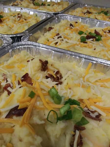 Creamy mashed potatoes in a tray, topped with bacon bits, more cheese, and green onions