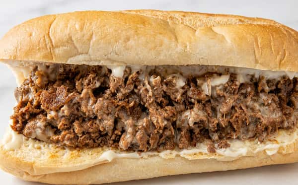 Philly cheesesteak sandwich on a soft hoagie roll, filled with chopped seasoned beef and melted cheese.