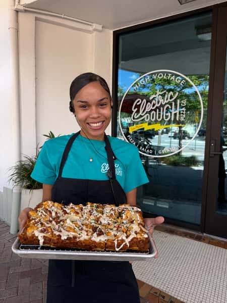 Image of smiling team member holding the September Pizza of the Month, the Electric Ranch