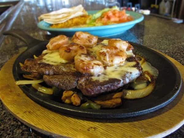 Steak and shrimp fajita dish served with a side of tortilla chips, guacamole and more salads