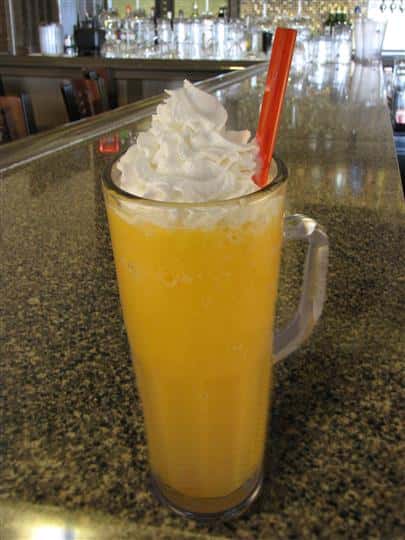 Cocktail drink served in tall pint glass topped with whipped cream and served up with a straw