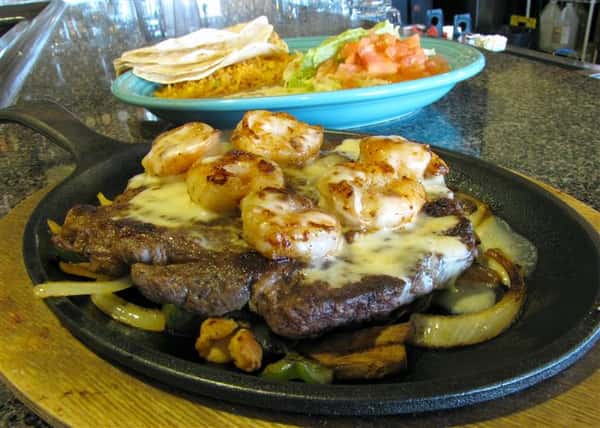 Steak and shrimp fajita dish served with a side of tortilla chips, guacamole and more salads