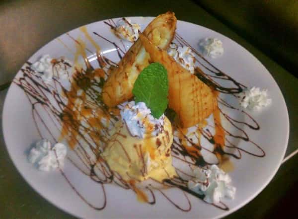 Dessert dish served with ice cream and whipped cream and decorated with syrup and a mint leaf