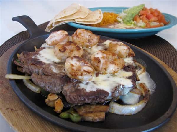 Steak and shrimp fajita dish served with a side of tortilla chips, guacamole and more salads