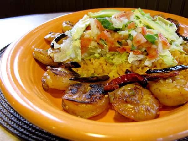 Grilled shrimp served with rice in the middle topped with shredded lettuce, tomato and onion