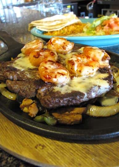 Steak and shrimp fajita dish served with a side of tortilla chips, guacamole and more salads