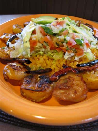 Grilled shrimp served with rice in the middle topped with shredded lettuce, tomato and onion