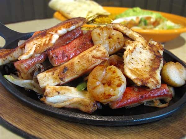 Seafood salad with a bed of lettuce topped with shrimp, scallops, onions, bell peppers and cheese.