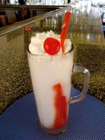 Cocktail drink served in tall pint glass topped with whipped cream and a cherry and served with a straw
