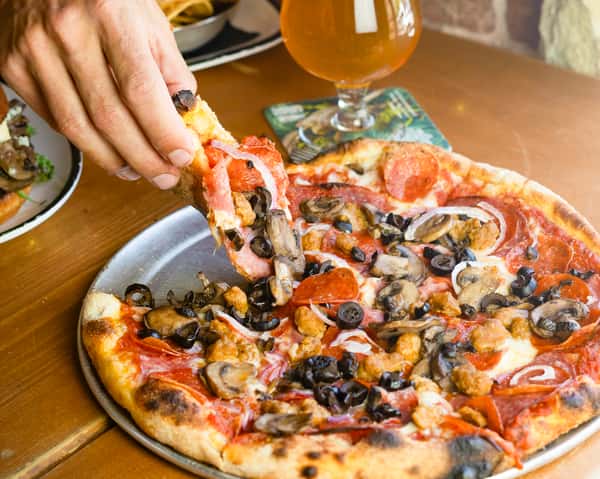 Hand pulling a slice of the capital city combo pizza out of a full pizza pie.
