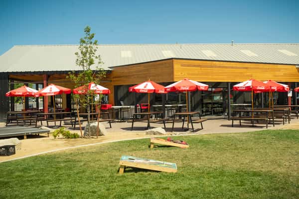 Minden patio with green grass, blue skies, red and white umbrellas and corn hole.