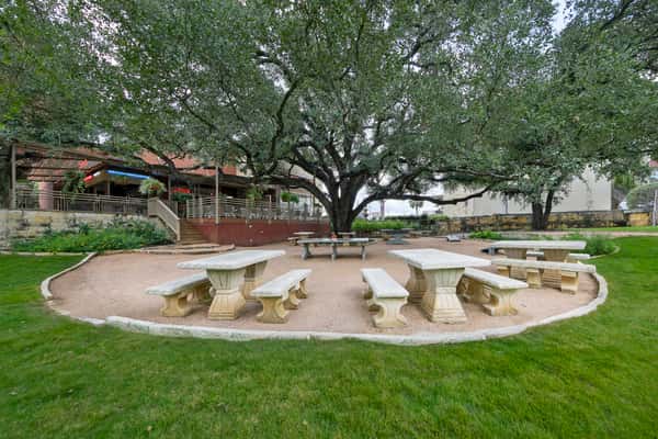 Outdoor courtyard dining area with stone picnic tables beneath large oak trees at a Mexican restaurant patio.