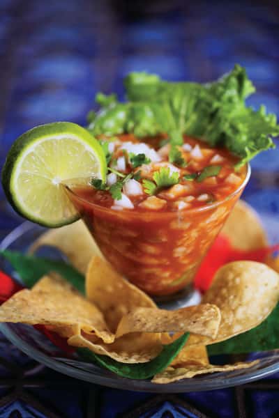 Shrimp cocktail served Mexican style with tomato-based sauce, lime garnish, cilantro, and tortilla chips.