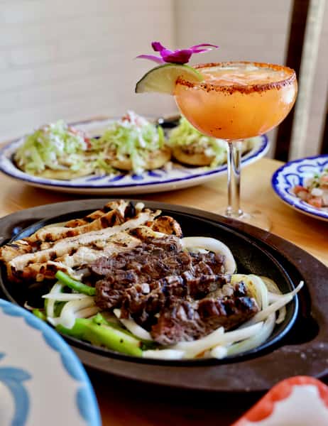 Classic Mexican fajita platter with grilled beef and chicken, sautéed onions and peppers, paired with a chili-rimmed margarita.
