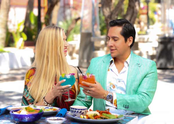Couple enjoying colorful margaritas at an outdoor Mexican restaurant, dining al fresco with vibrant plates of authentic cuisine in a relaxed, sunny patio setting.
