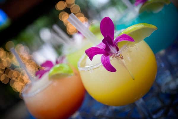 Bright frozen margaritas in assorted flavors, garnished with lime and purple orchids on a restaurant patio table.