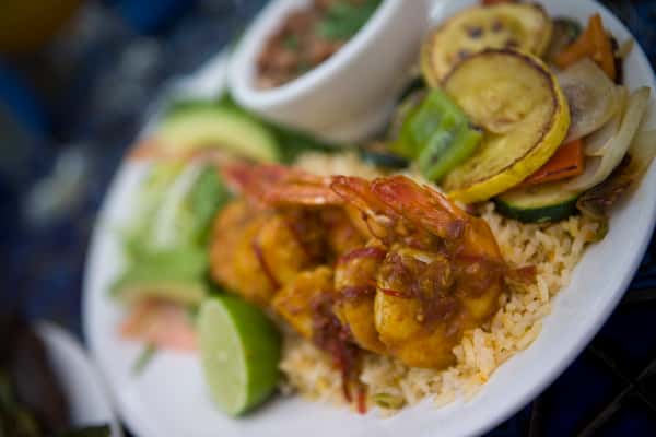 Mexican shrimp entrée with rice, sautéed vegetables, avocado, and salsa served on a white plate.