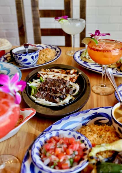 Sizzling Mexican fajitas with grilled steak and chicken served on a cast-iron skillet, surrounded by rice, beans, salsa, and margaritas.