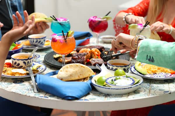 Friends sharing Mexican food and cocktails around a table with tortillas, fajitas, rice, beans, and margaritas.
