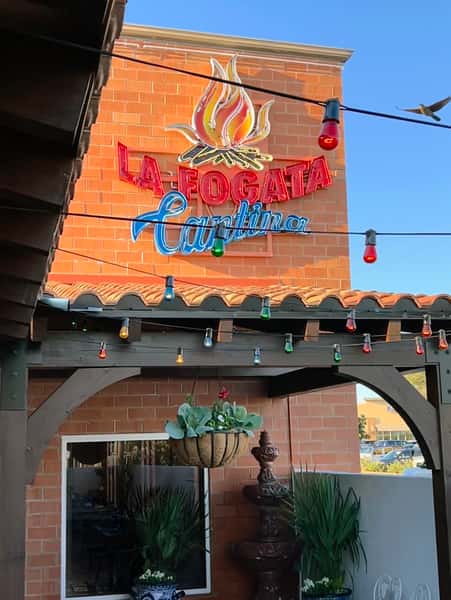 La Fogata Cantina neon sign mounted on brick exterior with colorful string lights and rustic Mexican décor.