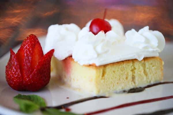 Tres leches cake topped with whipped cream, cherry, and fresh strawberry, served as a classic Mexican dessert.