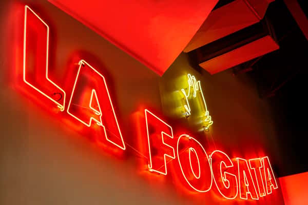 Red neon 'La Fogata' sign glowing inside a Mexican restaurant, creating a bold, vibrant atmosphere with modern lighting and nightlife energy.