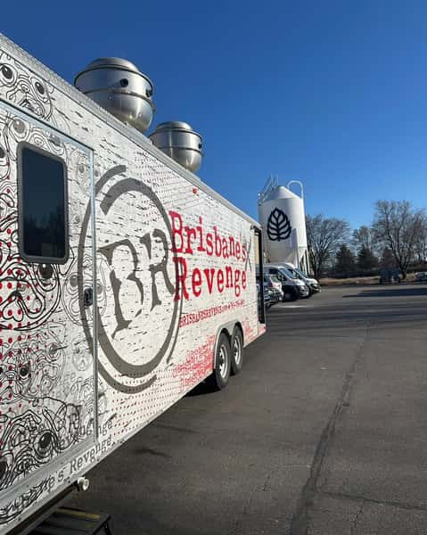 Brisbane's Revenge food truck parked near a brewery with fermenting silos in the background under a clear blue sky.