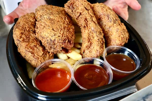 Four crispy fried chicken pieces served over fries with three dipping sauces: hot sauce, barbecue, and brown gravy.