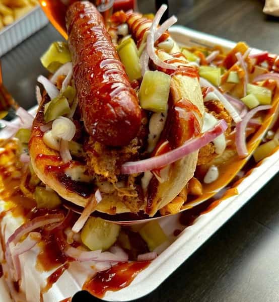 Loaded sausage sandwich topped with fried chicken, pickles, red onions, and drizzled with BBQ and ranch sauces.