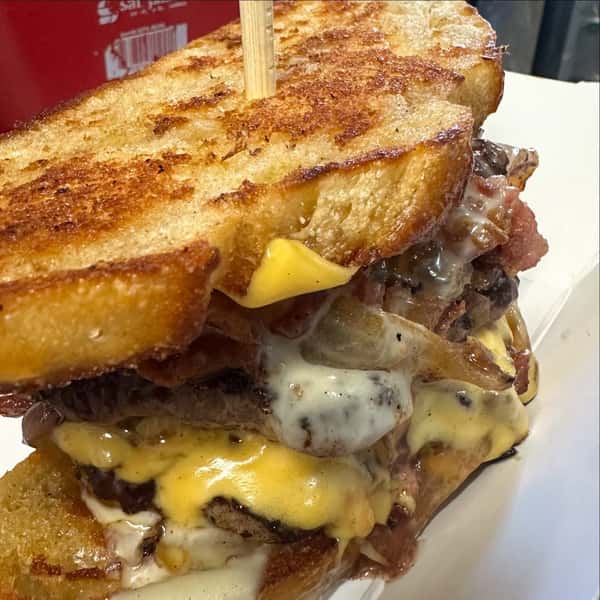 Close-up of a stacked grilled cheese burger with toasted bread, melted cheddar and mozzarella, beef patties, and bacon.