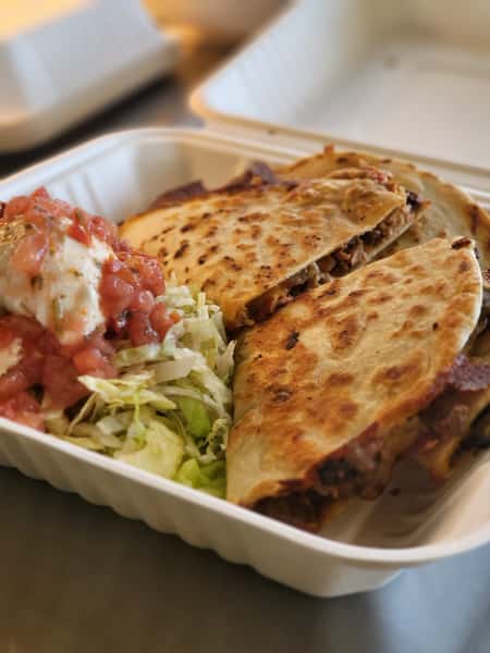 Grilled beef quesadillas with shredded lettuce, pico de gallo, and a dollop of sour cream in a takeout container.Grilled beef quesadillas with shredded lettuce, pico de gallo, and a dollop of sour cream in a takeout container.