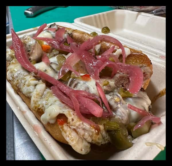 Pulled pork sandwich smothered in barbecue sauce with a soft bun, served in a takeout container with a side of pickles.