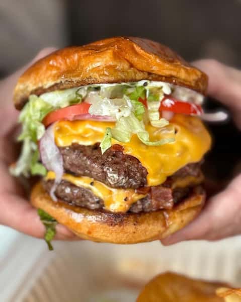 Double cheeseburger with lettuce, tomato, onion, and sauce on a toasted bun, held with both hands.