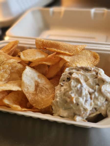 Crispy kettle chips served with a generous portion of creamy French onion dip in a white takeout container.