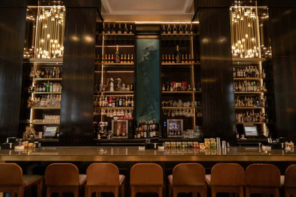 Chic upscale bar with backlit liquor shelves, pendant lighting, and a long counter lined with tan leather barstools.
